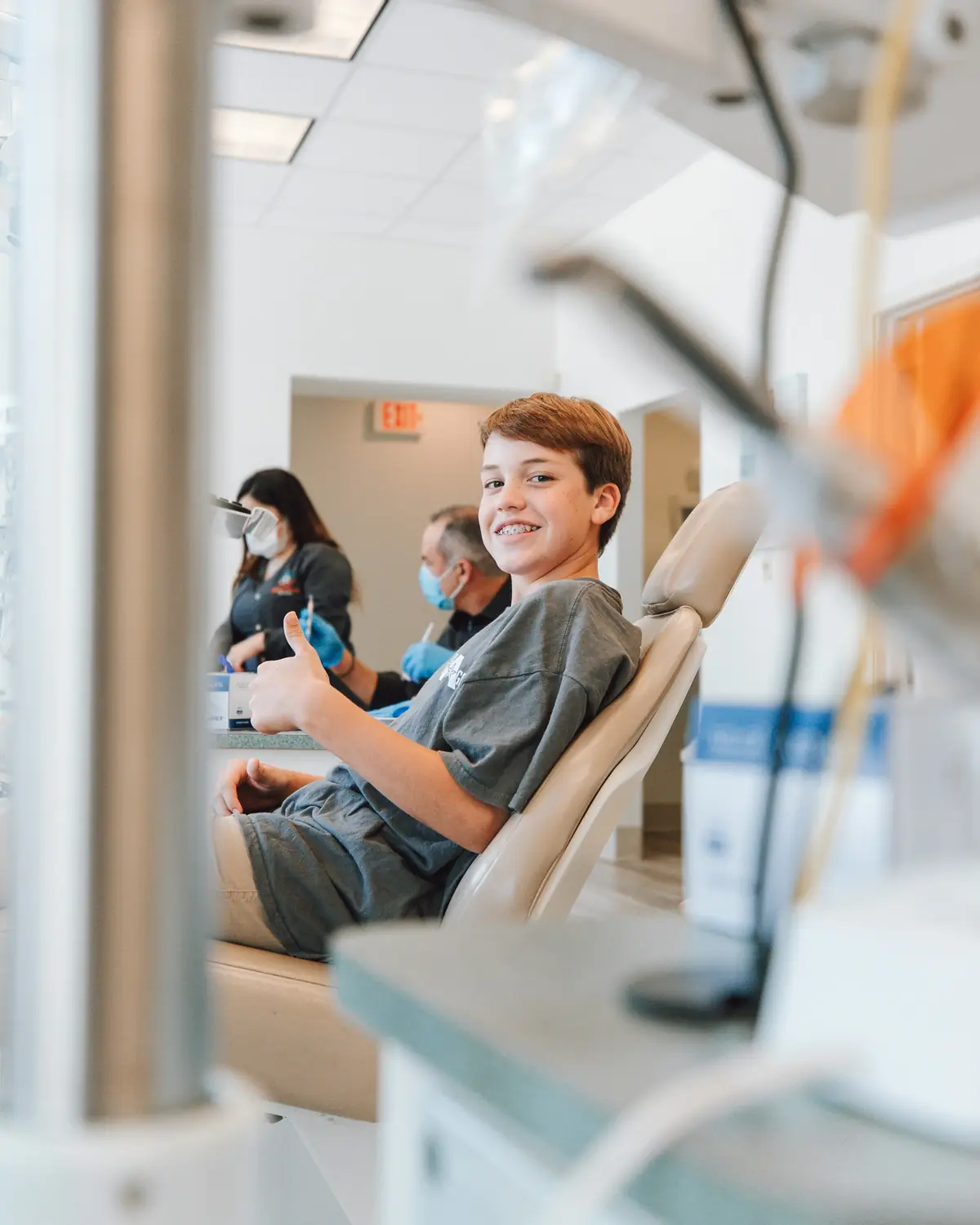 A smiling boy giving a thumbs up from a dental chair